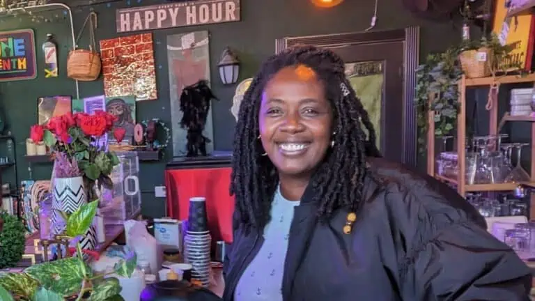 A woman poses behind a bar with flowers and more decor on the walls