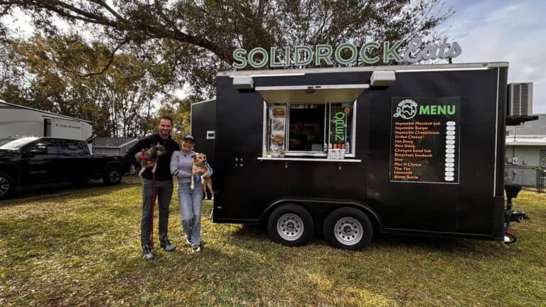 two people holding a pup stand next to a black and green food truck outside