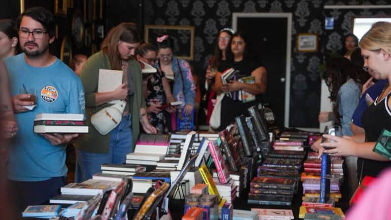 A group of people browsing and selecting books from tables filled with colorful displays at a book fair.