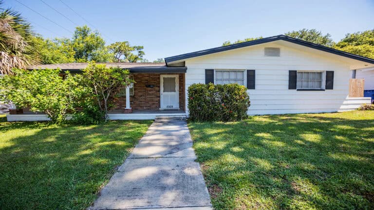 exterior of historic home with green grass and paved walkway leading to door.