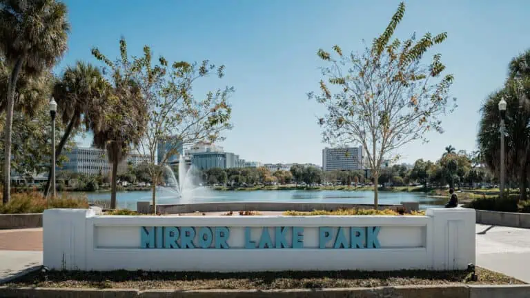 sign that says "mirror lake park" with lake and building in background