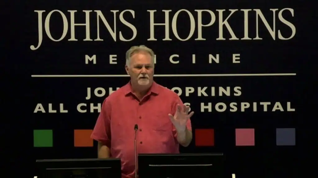 red-shirted man man speaking in front of a black background.