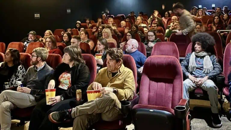 a group of people watch a film in a theatre. many are enjoying concessions while viewing the film