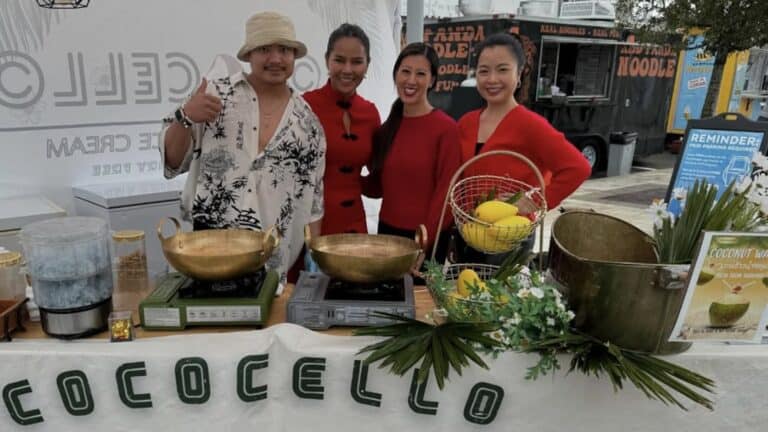 A group of people behind a table at an outdoor market event. Bowls of vegan ice cream are displayed on the table