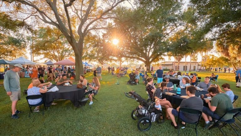 people eat and drink at picnic tables at a local park