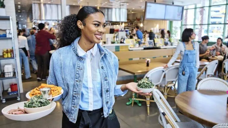 a person in a denim jacket and white button down shirt holds multiple plates of food