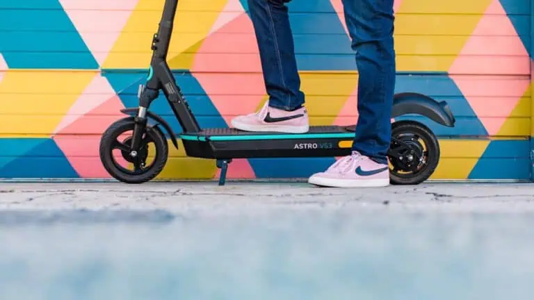 someone with pink shoes poses on an electric scooter. Only the bottom portion of the electric scooter is in the shot