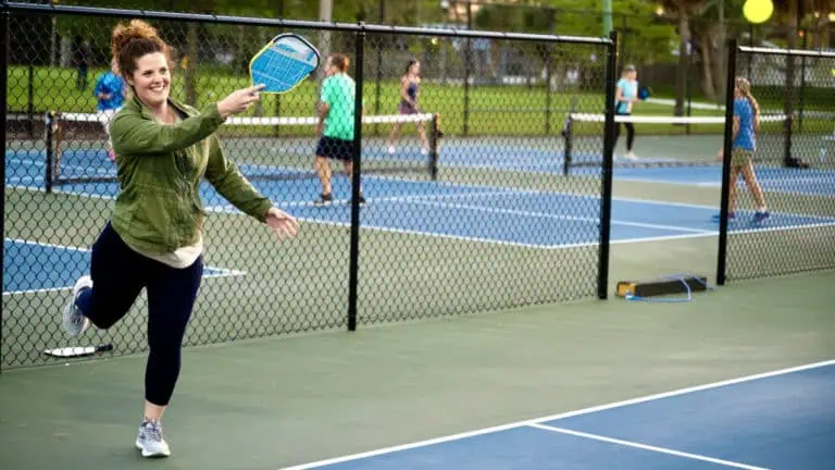 A woman plays tennis on a court with several other players in the background, enjoying a sunny day.