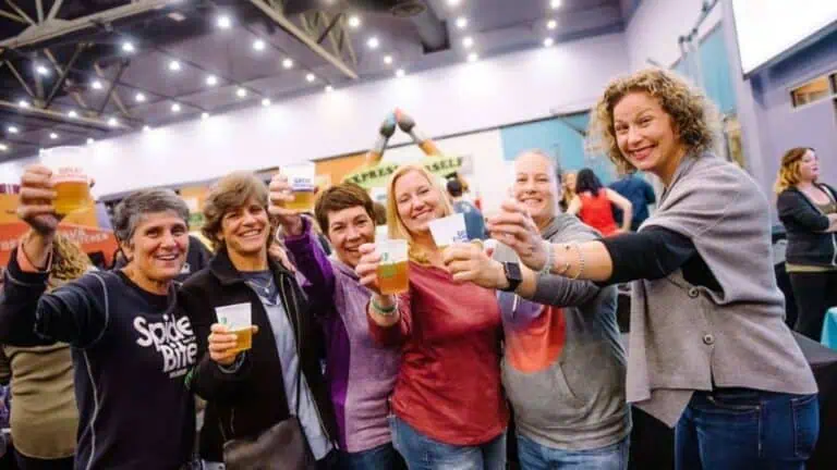A group of women joyfully raising their beers together at a lively event, celebrating and having a great time.