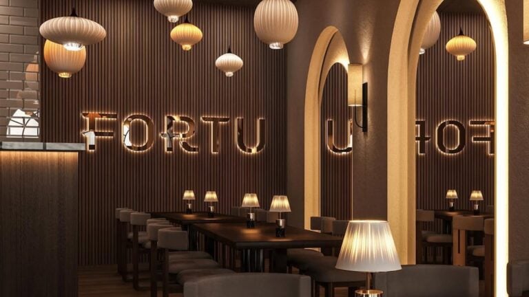 interior of Fortu Restaurant in St. Pete. The interior is filled with chic chandeliers and soft lighting around wooden tables. The name "Fortu" is illuminated