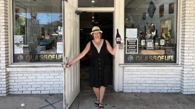 woman standing out front of door holding wine bottle