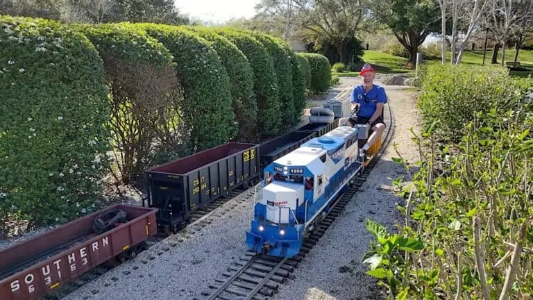 a person riding a small train. It's blue and white on one of three tracks in a park