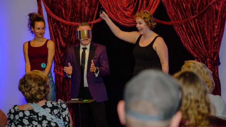 Joshua Seth in between two women on the stage while blindfolded