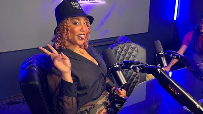 REE BABY, an artist is on set for a podcast. She's wearing a black bucket hat, and sits in front of a microphone