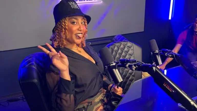 REE BABY, an artist is on set for a podcast. She's wearing a black bucket hat, and sits in front of a microphone