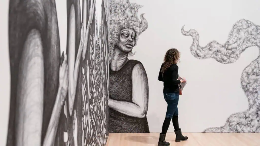 a person walks through an art gallery with black and white illustrations of women with flowing hair on the walls