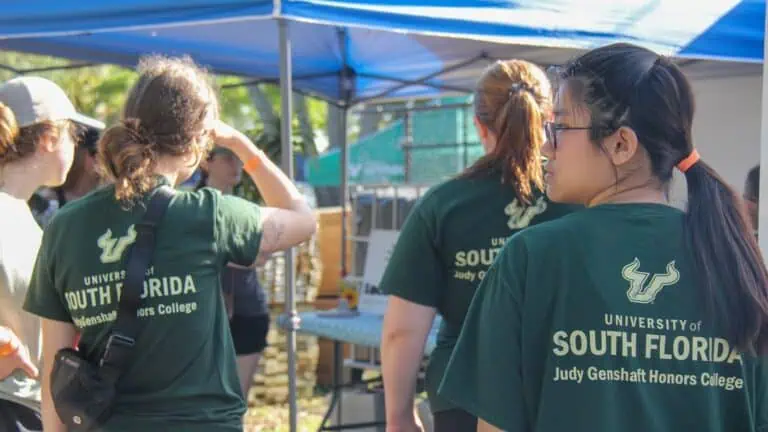 Three college students in gold and green shirts volunteer at Youth Farm event and assist with compost education for attendees
