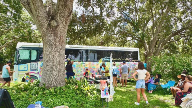 a group of people around a the NOMAD art bus. this is a community painting event at a park on a sunny day