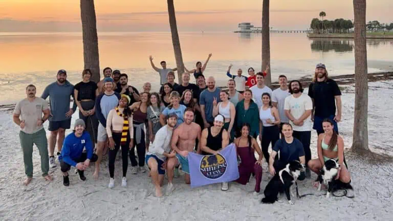 A group of people pose for the camera at a beach during sunrise.