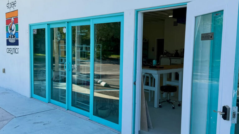 The freshly repainted St. Pete Ceramics storefront, with turquoise-framed glass doors, a left-side logo, and an open front door showing work tables, stools, and shelving inside.
